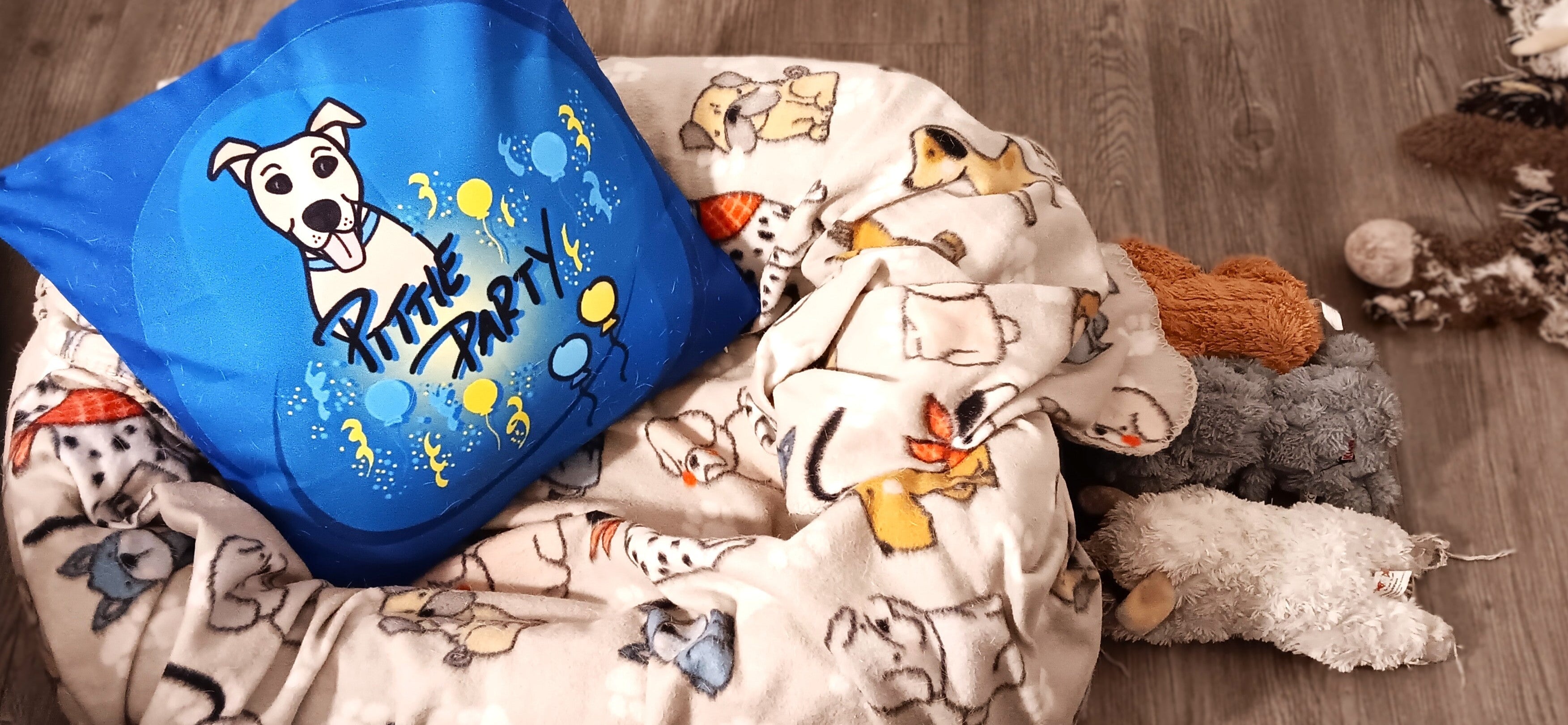Throw pillow with cartoon dog design and a blanket with dog pattern on a wooden floor.